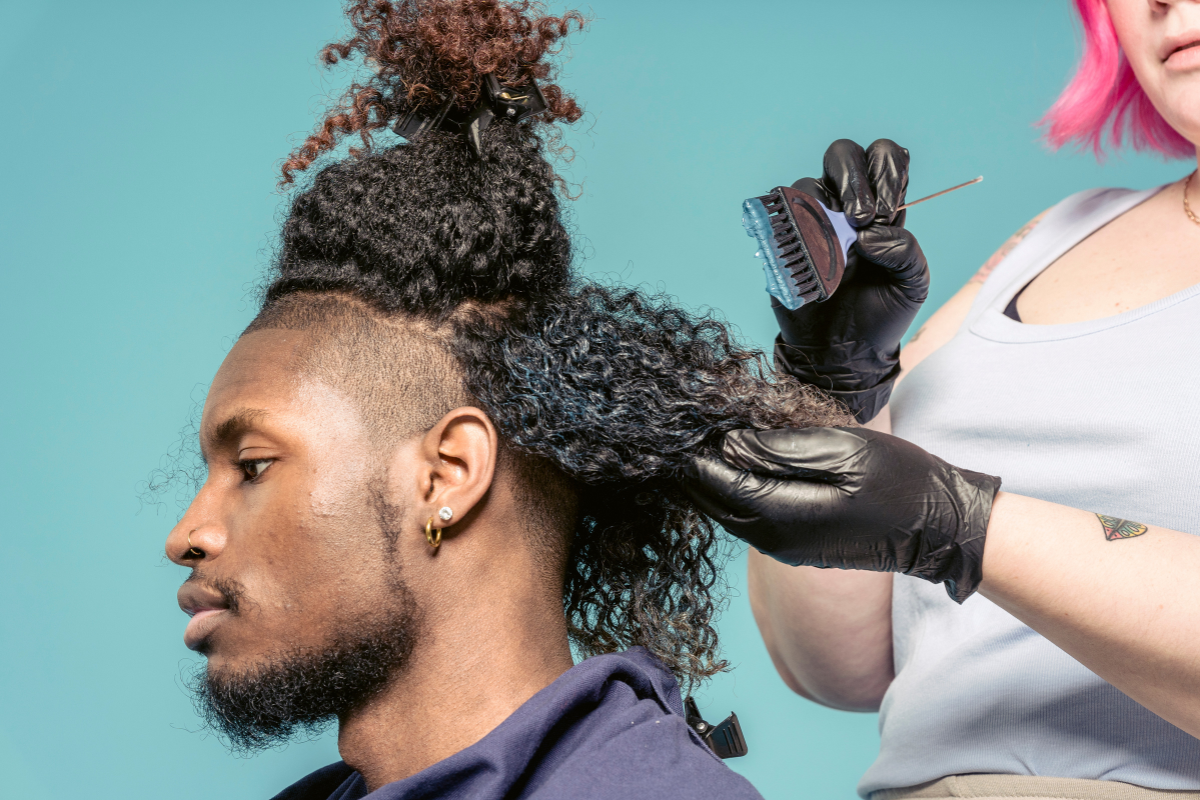 A barber applying petroleum jelly along a client’s hairline before dyeing
